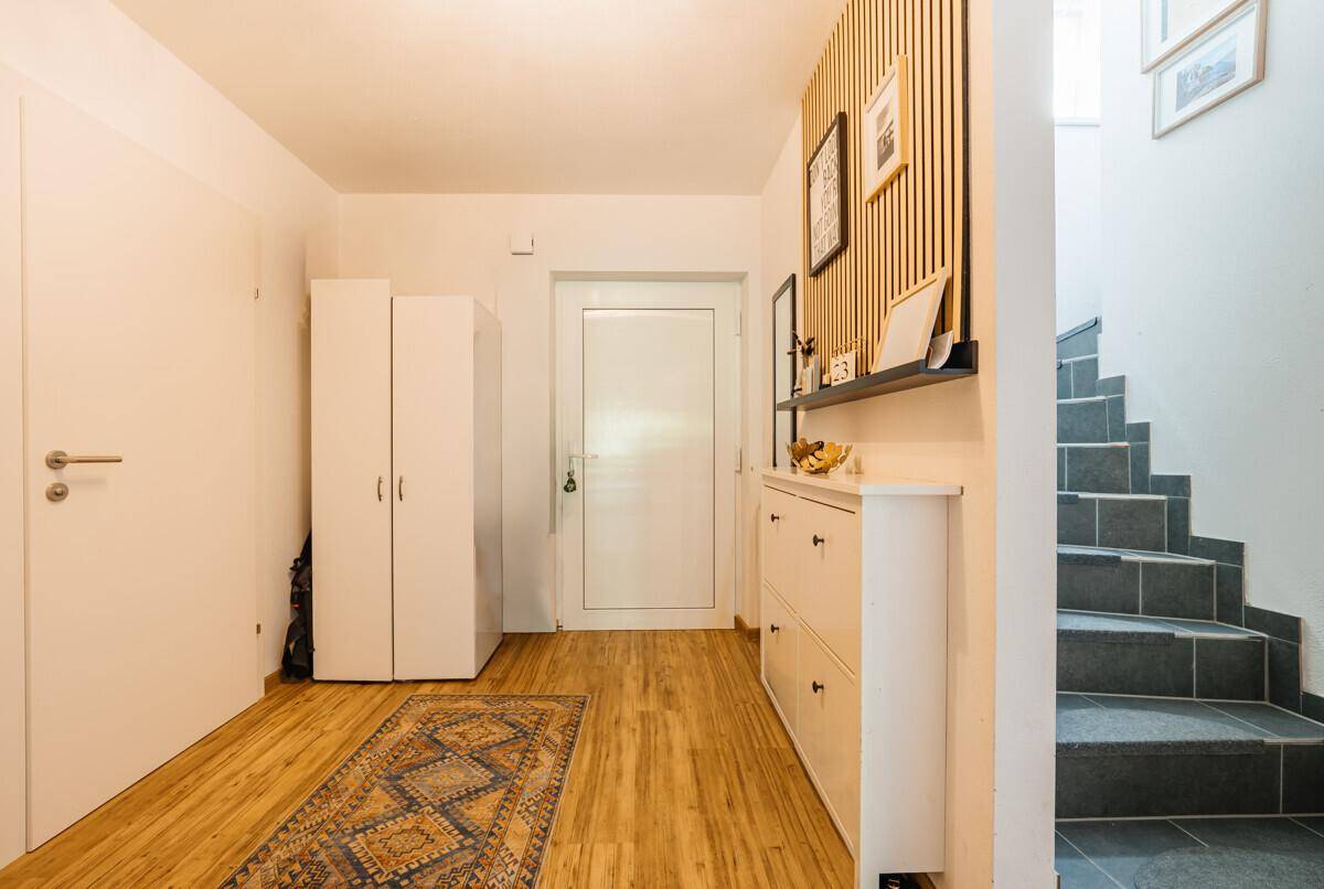 Heller Eingangsbereich mit Holzfußboden, modernem Schuhschrank und einer Treppe mit dunklen Fliesen.