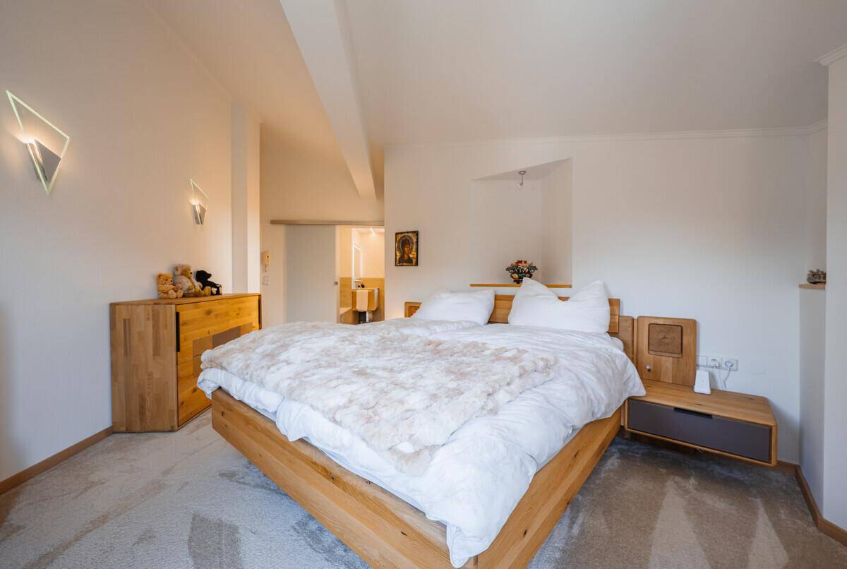Geräumiges Schlafzimmer mit Holzbett, Teppichboden und Zugang zum Badezimmer.