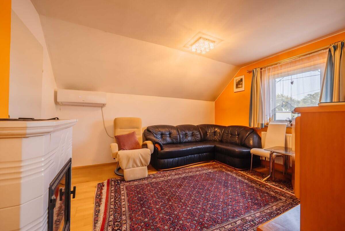 Gemütliches Dachgeschoss-Wohnzimmer mit Kamin, Ledersofa und schrägen Wänden.