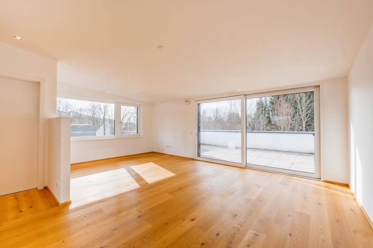 Geräumiger, heller Raum mit Holzboden, großen Schiebetüren und Zugang zu einer Terrasse.