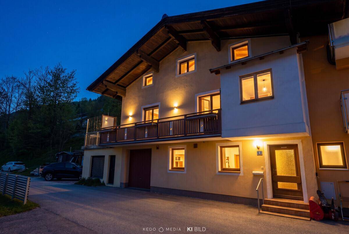 Das Haus bei Nacht mit beleuchteten Fenstern und Balkonen, umgeben von Bäumen.