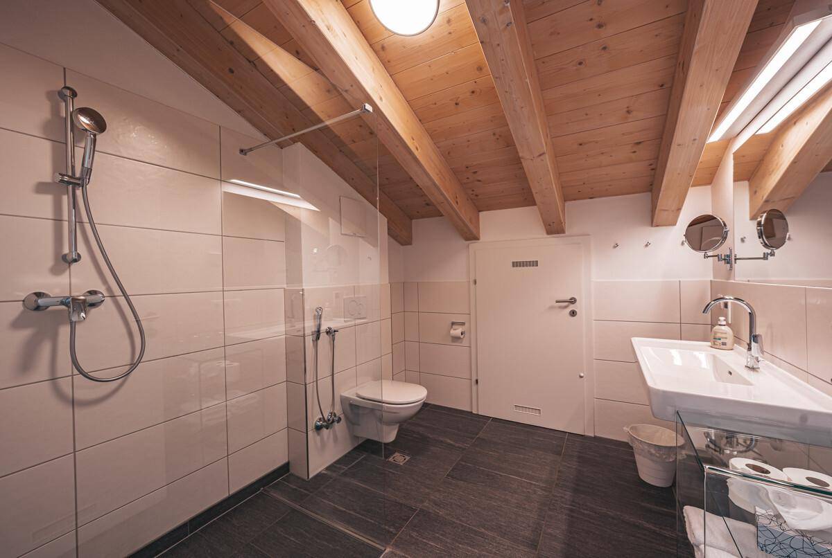 Modernes Badezimmer mit Duschkabine, wandhängendem WC und Waschbecken unter Holzbalkendecke.