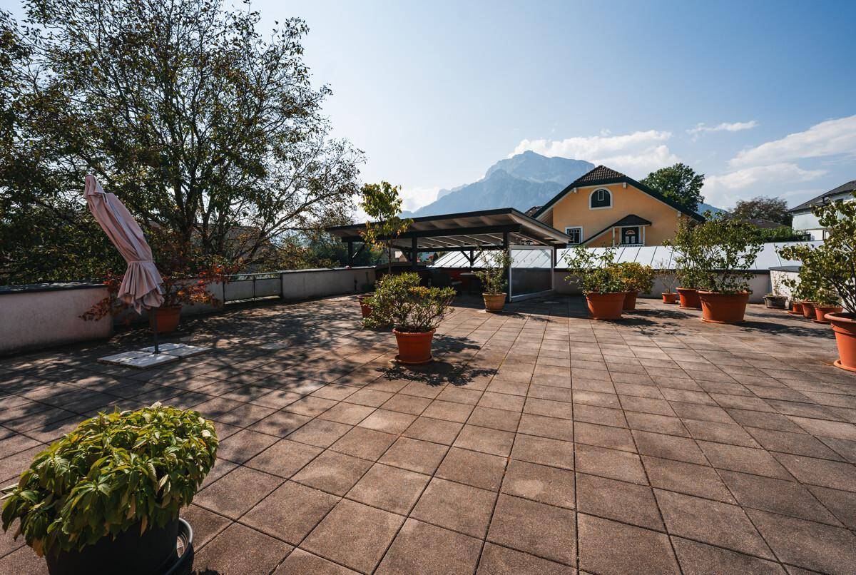 Große gepflasterte Terrasse mit Topfpflanzen, Sonnenschirm und Bergblick.