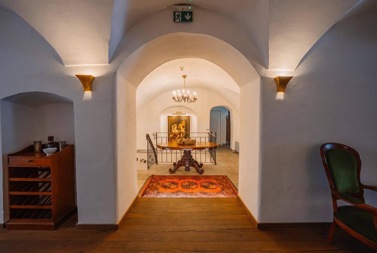 Historischer Flur mit Gewölbedecken, Holzboden und Blick auf eine elegante Treppe.