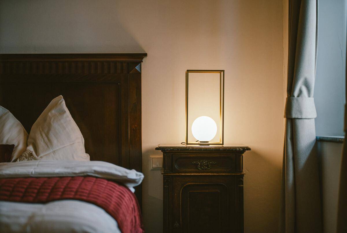 Nachttisch mit moderner Lampe neben einem traditionellen Holzbett und Vorhängen.