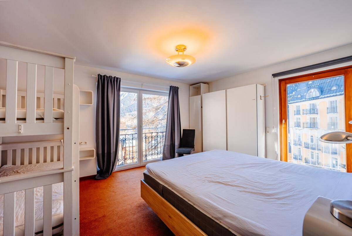 Schlafzimmer mit Doppelbett, Etagenbett und französischem Balkon mit Blick auf die Berge.