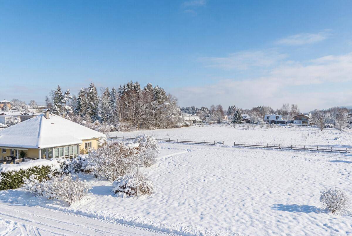Verschneite Landschaft mit weiten Feldern und Wäldern unter einem klaren Winterhimmel.