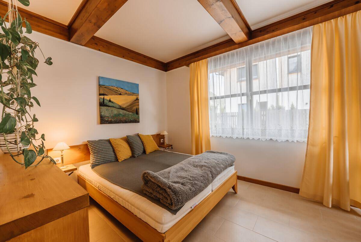 Gemütliches Schlafzimmer mit Holzbalkendecke, Doppelbett und gelben Vorhängen.