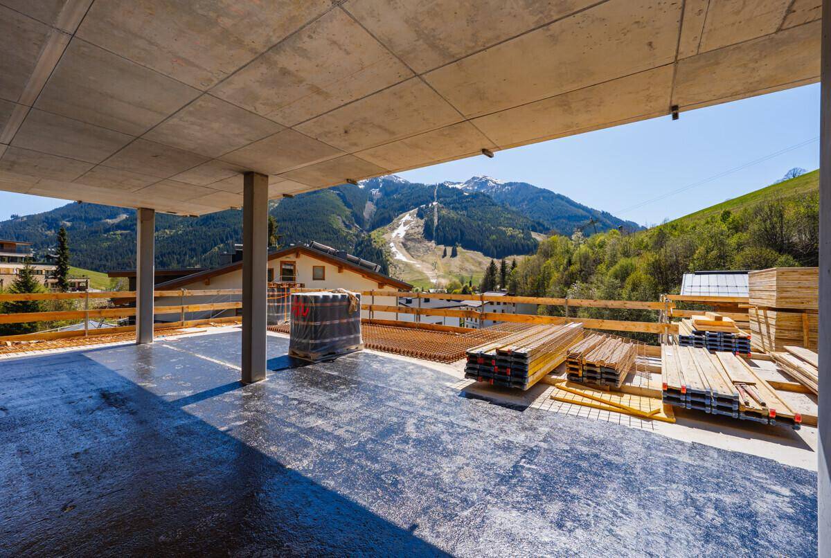 Baustelle mit einer großen Betonterrasse und Baumaterialien, umgeben von einer Berglandschaft.