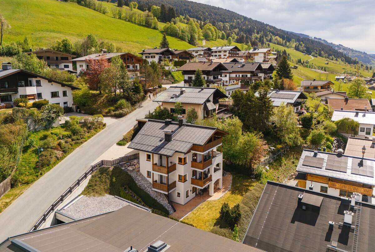 Panoramablick auf ein idyllisches Bergdorf, umgeben von grünen Hügeln und Wäldern.