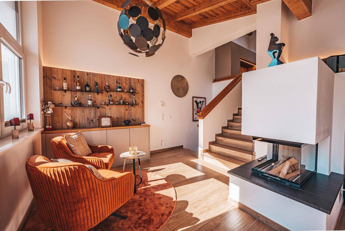 Heller Wohnbereich mit Kamin, Bar, zwei Sesseln und Treppe zum Obergeschoss.