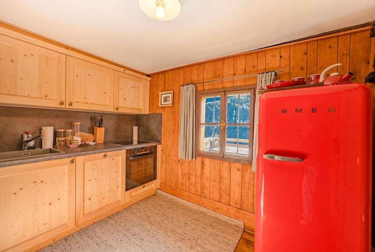 Rustikale Küche mit Holzeinbauten, modernem Backofen und einem auffälligen roten Kühlschrank.