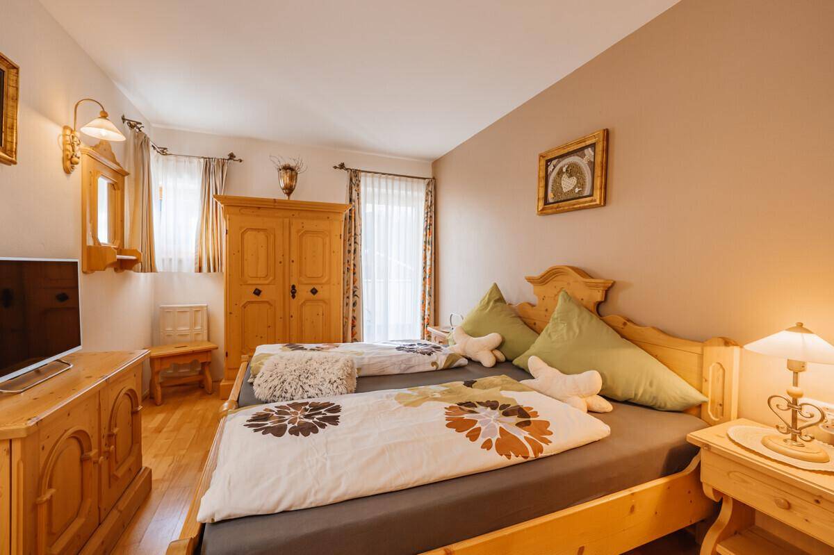 Schlafzimmer mit zwei Einzelbetten, Holzmöbeln und Zugang zu einem Balkon.
