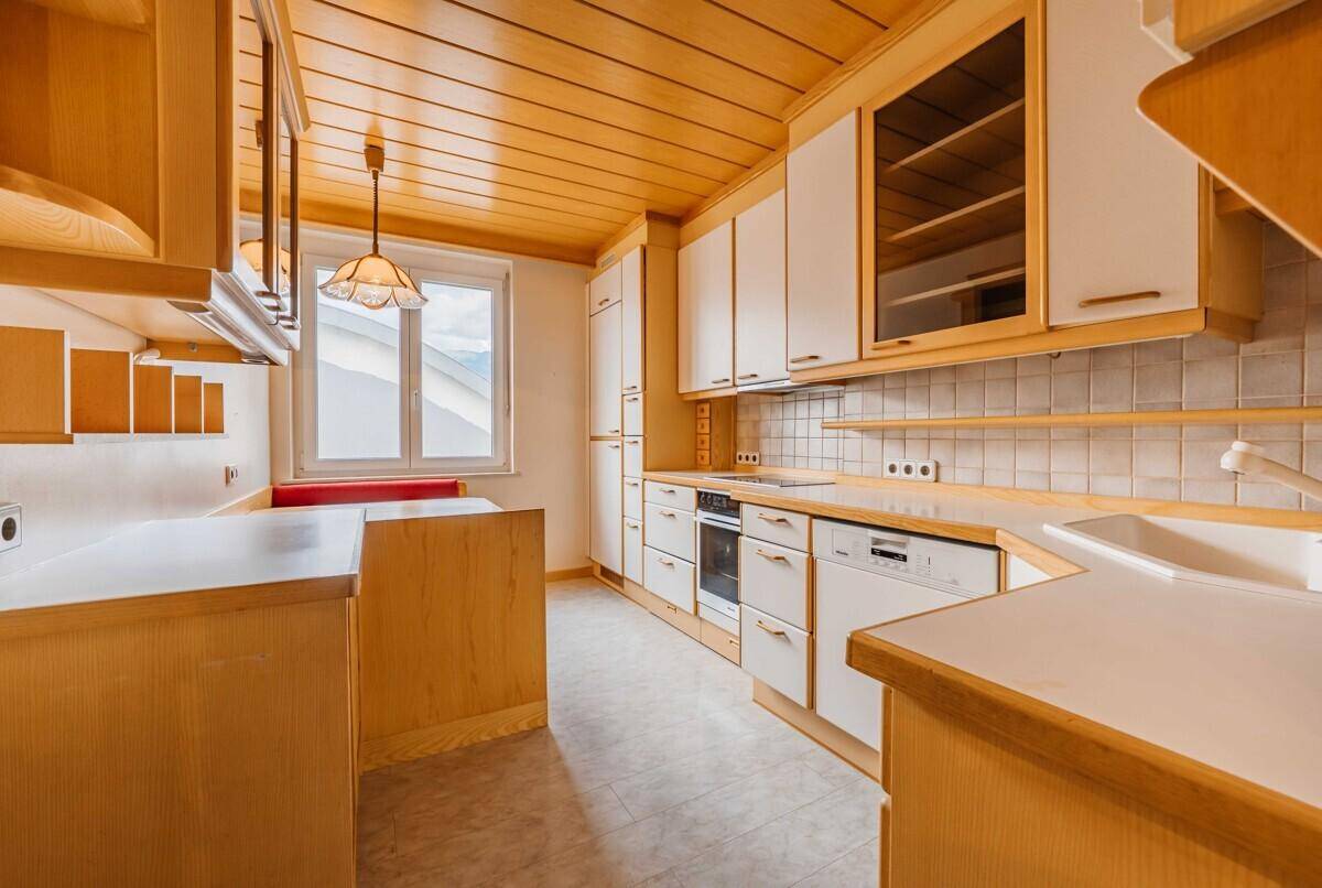 Helle Küche mit Holzbalkendecke, weißen Schränken und integrierten Geräten, inklusive Essbereich.
