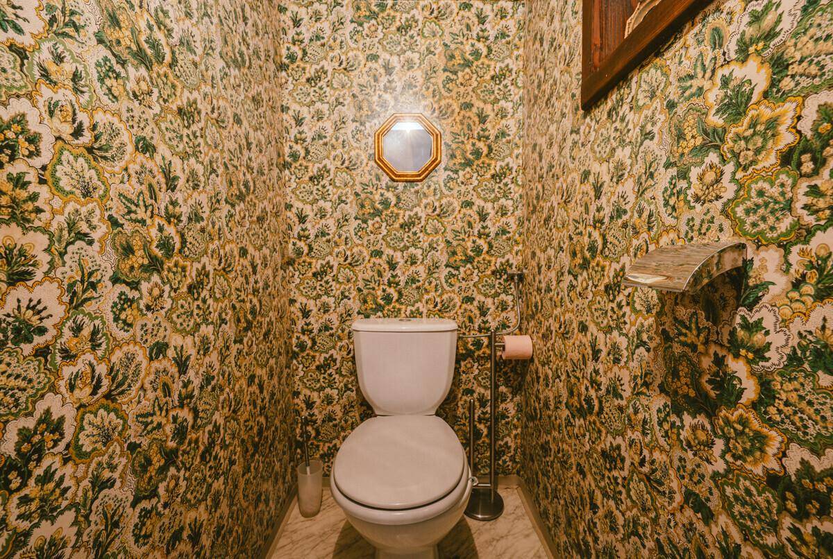 Kleines WC mit auffälliger, gemusterter Tapete und einem runden Spiegel.
