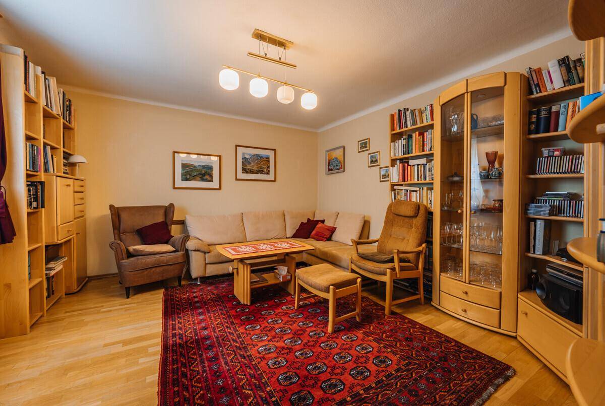 Helles Wohnzimmer mit beigem Sofa, Bücherregalen und einem traditionellen Teppich auf Holzparkett.