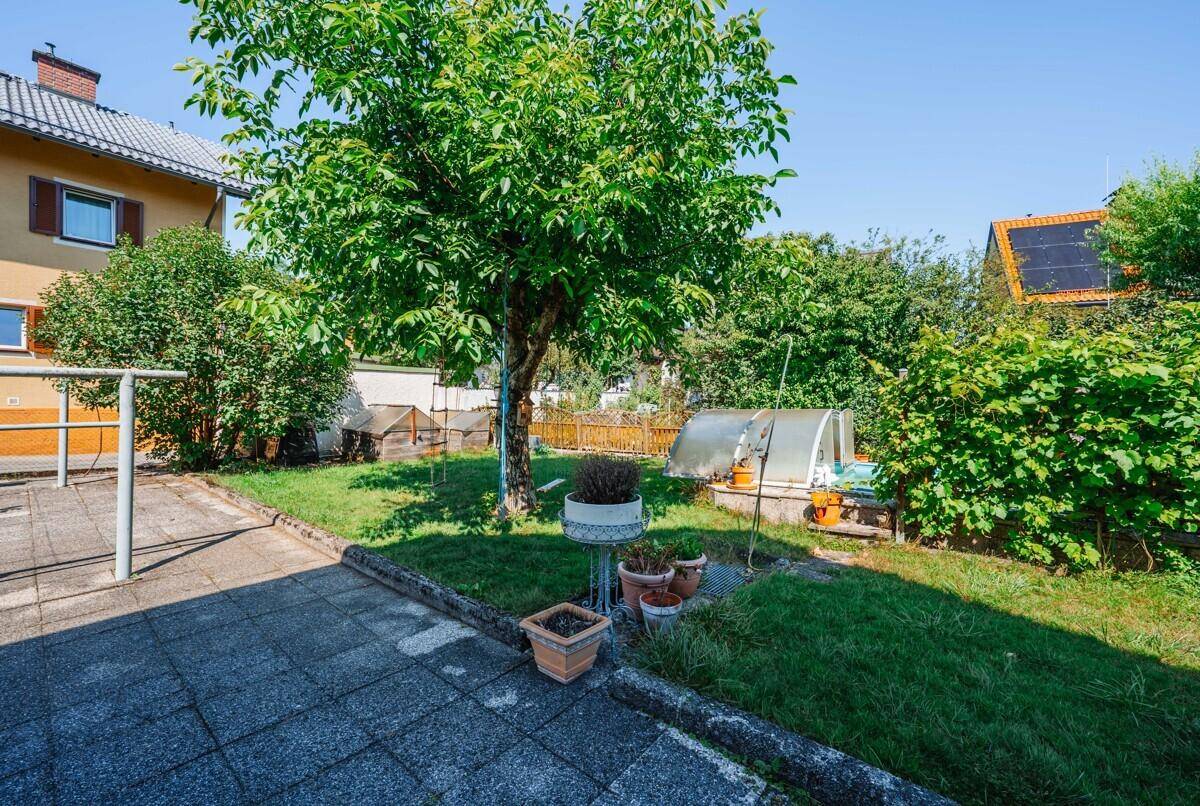Gepflegter Gartenbereich mit Rasen, Bäumen und einem gepflasterten Weg neben dem Haus.