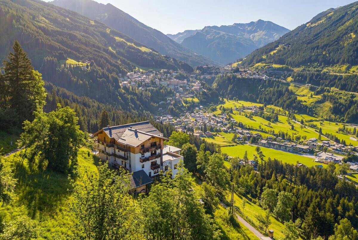 Panoramablick auf ein Gebäude in den Bergen, umgeben von grünen Tälern und einem Dorf in der Ferne.