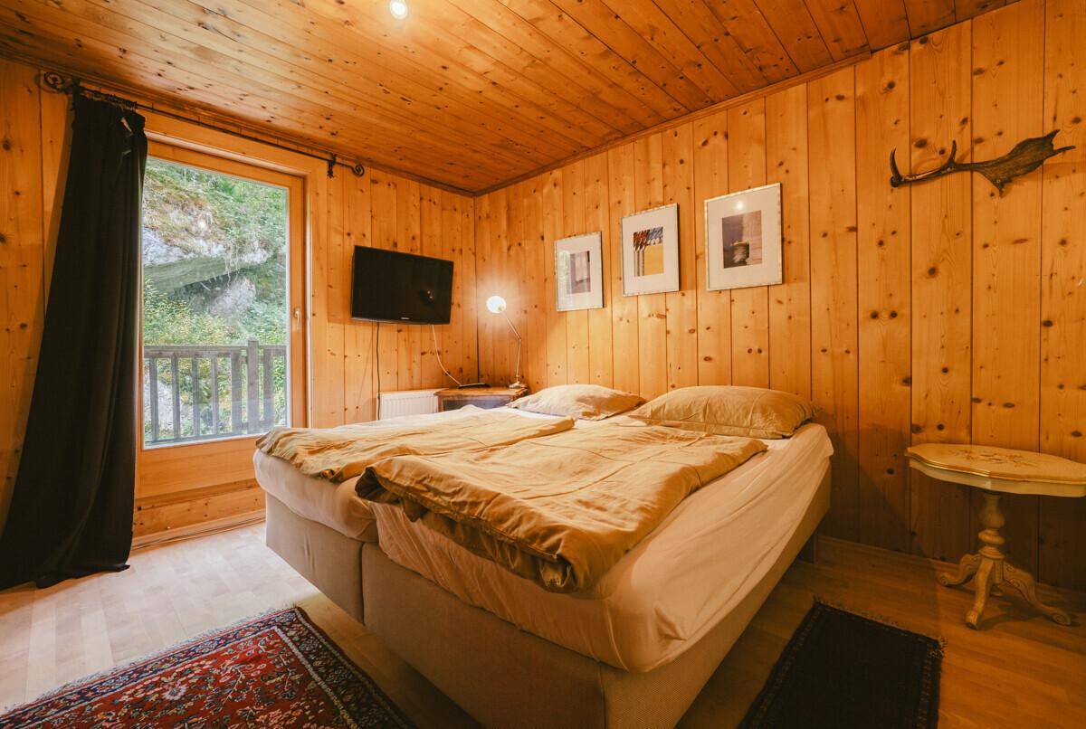 Rustikales Schlafzimmer mit Holzvertäfelung, Holzboden und Zugang zu einem kleinen Balkon.
