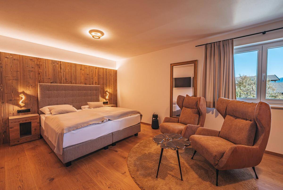 Schlafzimmer mit Holzwand, Doppelbett, zwei Sesseln und Holzboden.