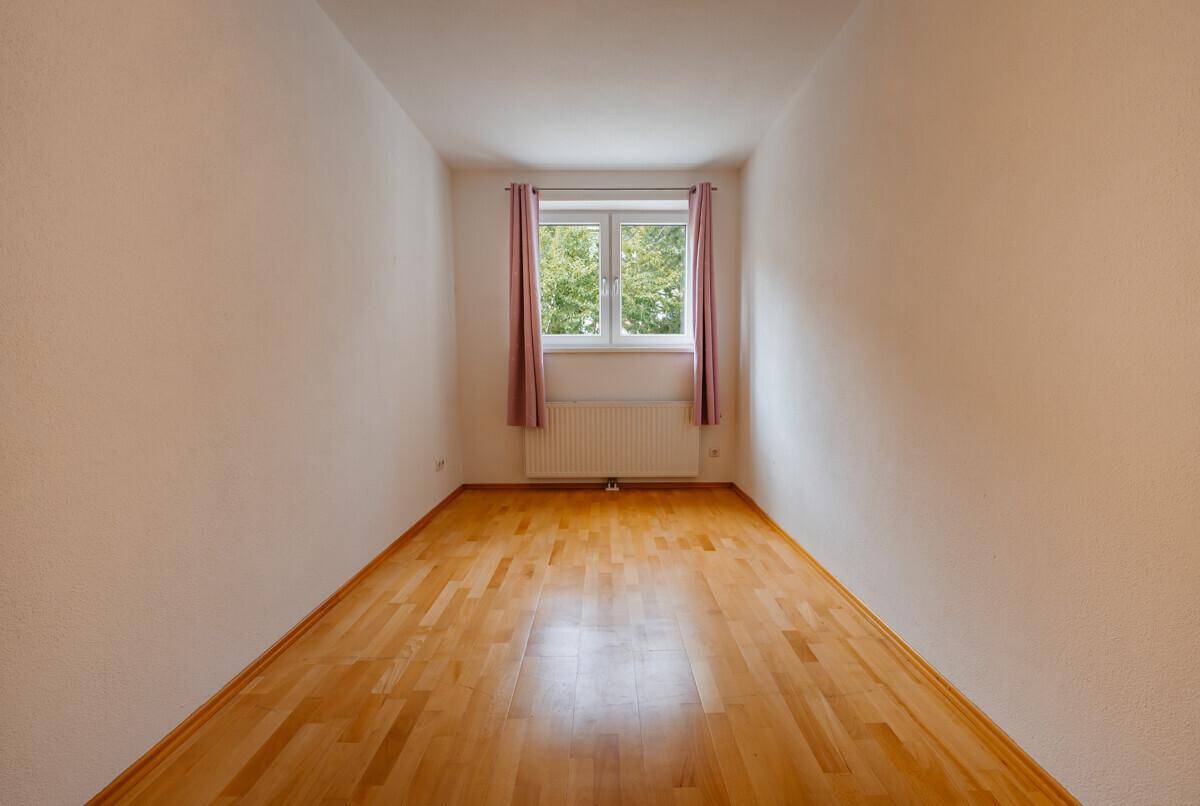 Helles Zimmer mit Parkettboden und Fenster, bereit zur individuellen Gestaltung.