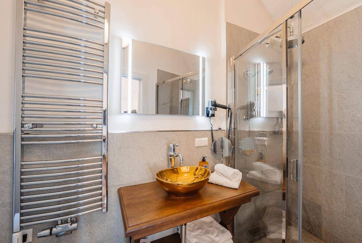 Badezimmer mit modernem Design, beheiztem Handtuchhalter und goldenem Waschbecken.