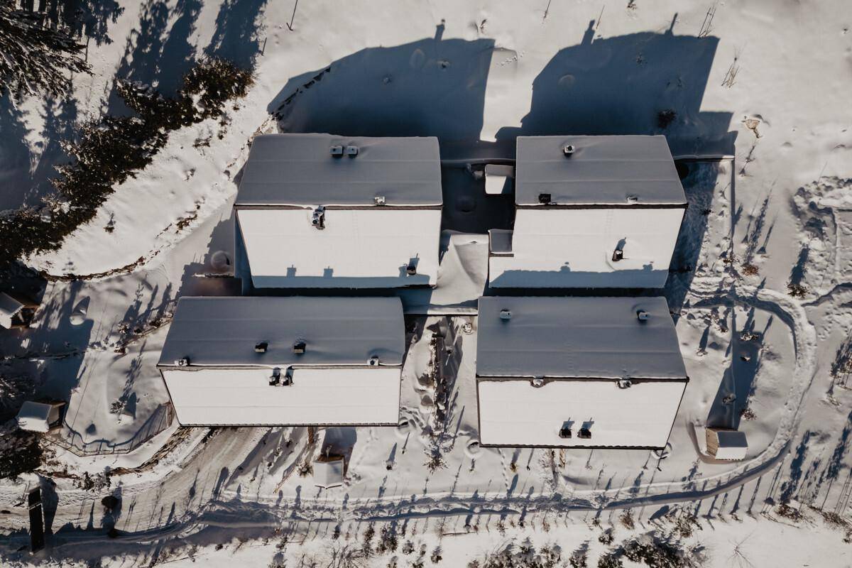 Luftaufnahme von mehreren Gebäuden mit verschneiten Dächern in winterlicher Umgebung.