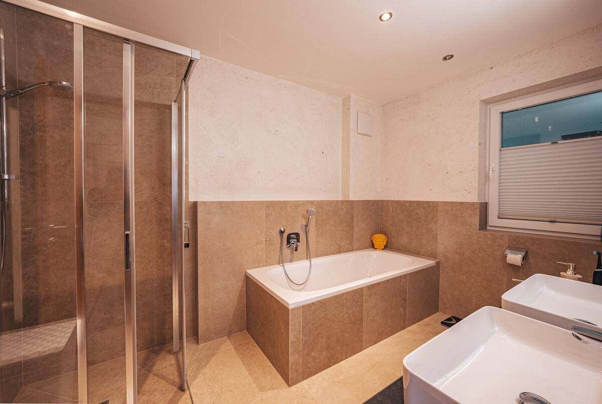 Badezimmer mit Badewanne, Dusche, Doppelwaschbecken und Fenster.