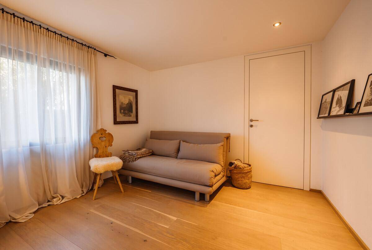 Helles Gästezimmer mit Holzboden, Schlafsofa und Fenster mit Vorhängen, gemütlich und funktional.