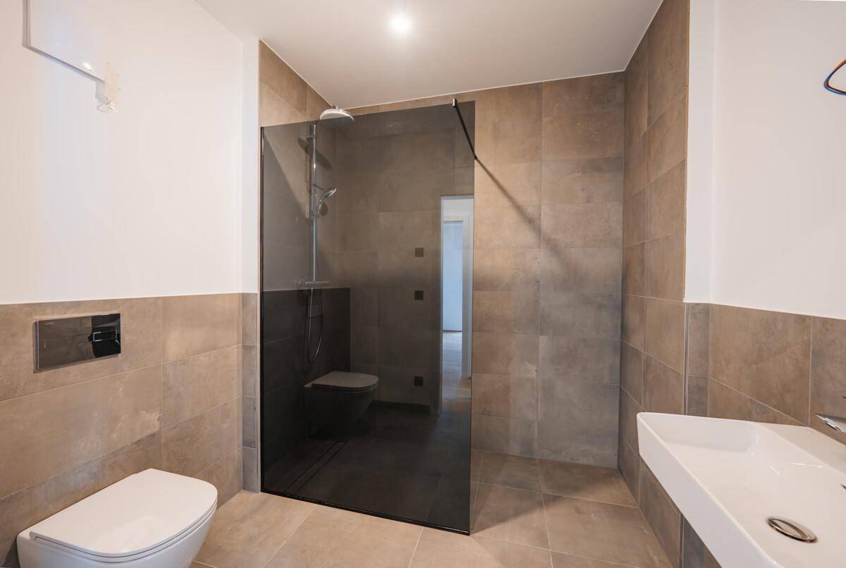 Modernes Badezimmer mit großformatigen Fliesen, bodengleicher Dusche und Wand-WC.