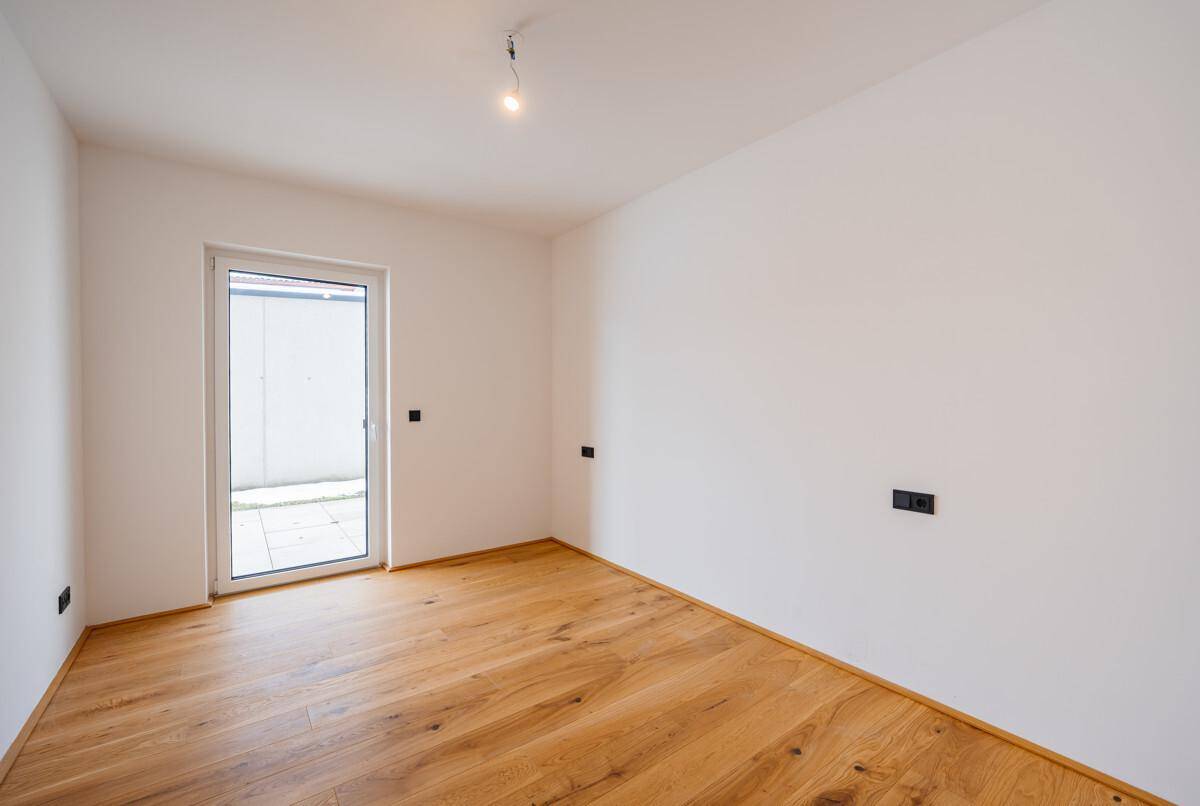 Leeres Zimmer mit Holzboden und Zugang zu einem kleinen Außenbereich, ideal als Schlafzimmer.