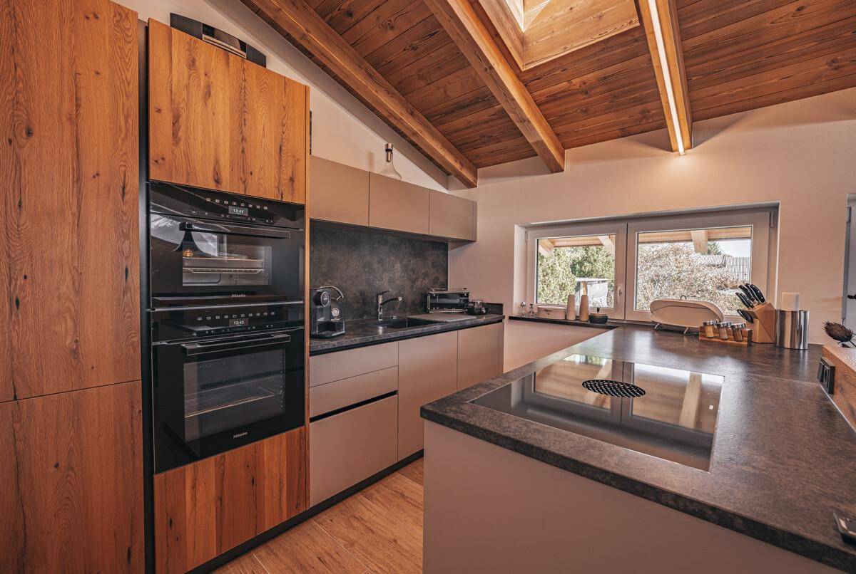 Moderne Küche mit Holzelementen, Einbaugeräten, Kochinsel und Holzbalkendecke.