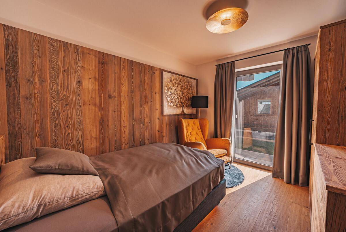 Schlafzimmer mit Einzelbett, Holzwand, Sessel und Zugang zum Balkon.