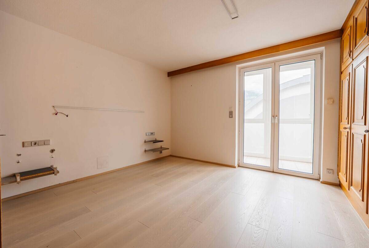 Helles Schlafzimmer mit hellem Laminatboden, Einbauschränken und Zugang zu einem französischen Balkon.