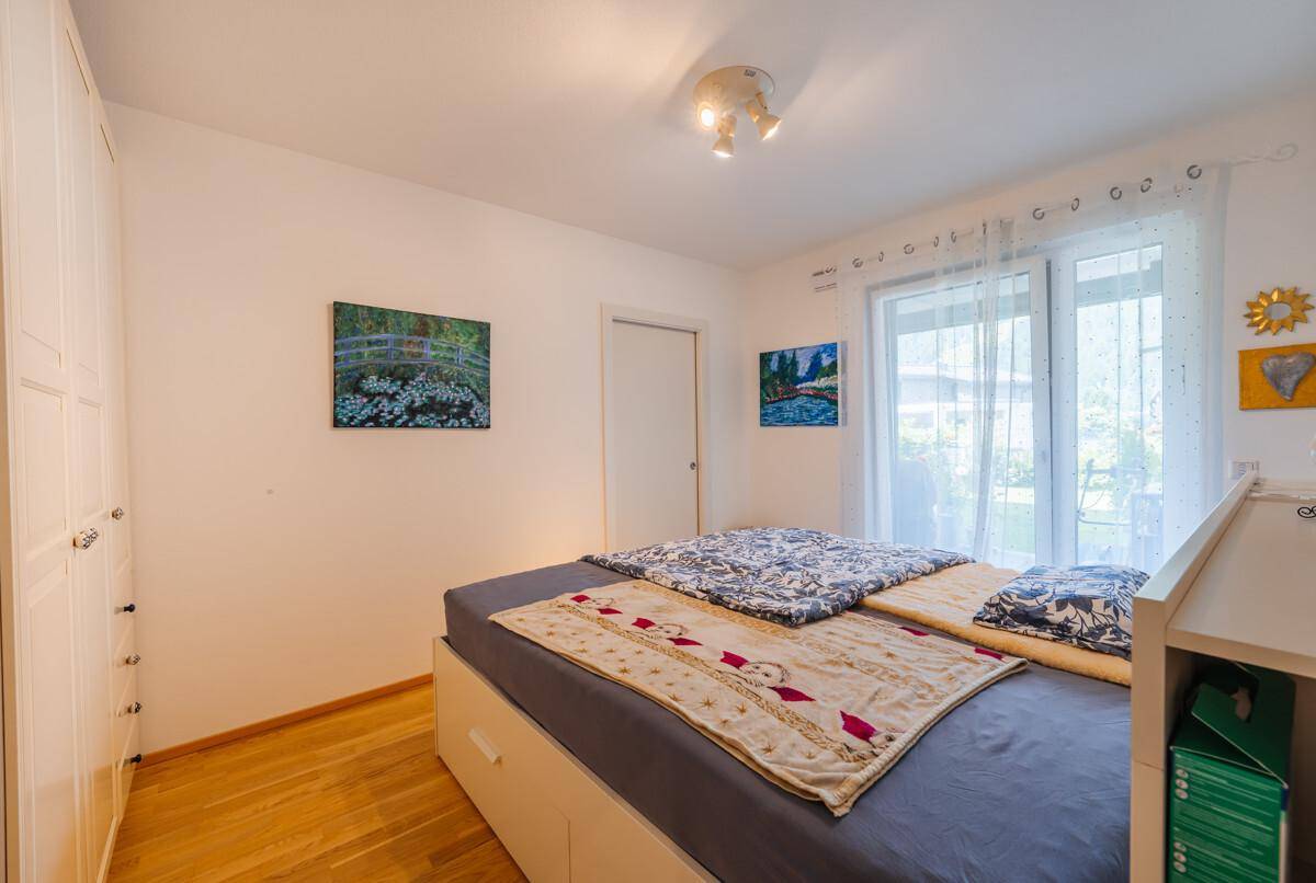 Helles Schlafzimmer mit Doppelbett, weißem Kleiderschrank und Fenster, das viel Tageslicht hereinlässt.