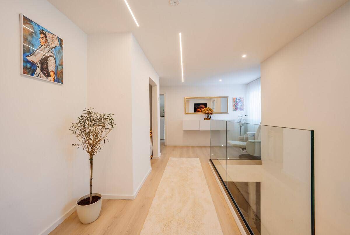 Moderner Flur mit heller Einrichtung, Kunstwerk und Glasgeländer zur Treppe.