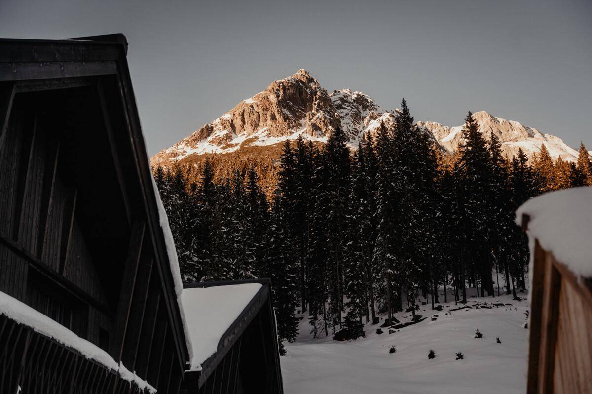Majestätischer Berggipfel in der Abendsonne, umgeben von dichtem Nadelwald und Schnee.