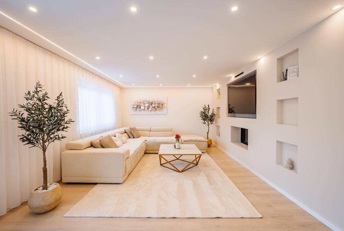 Gemütliches Wohnzimmer mit großem Ecksofa, hellem Teppich und indirekter Beleuchtung.