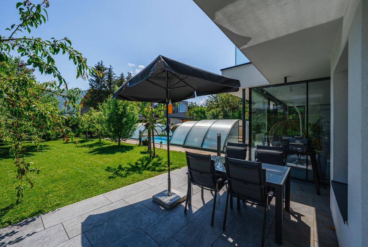 Sonnenterrasse mit Gartenmöbeln und Blick auf den Pool und den grünen Garten.
