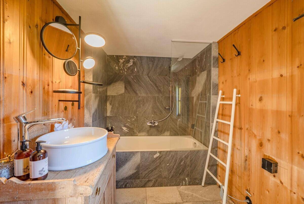 Badezimmer mit Holztäfelung, Badewanne mit Dusche und modernem Waschbecken.
