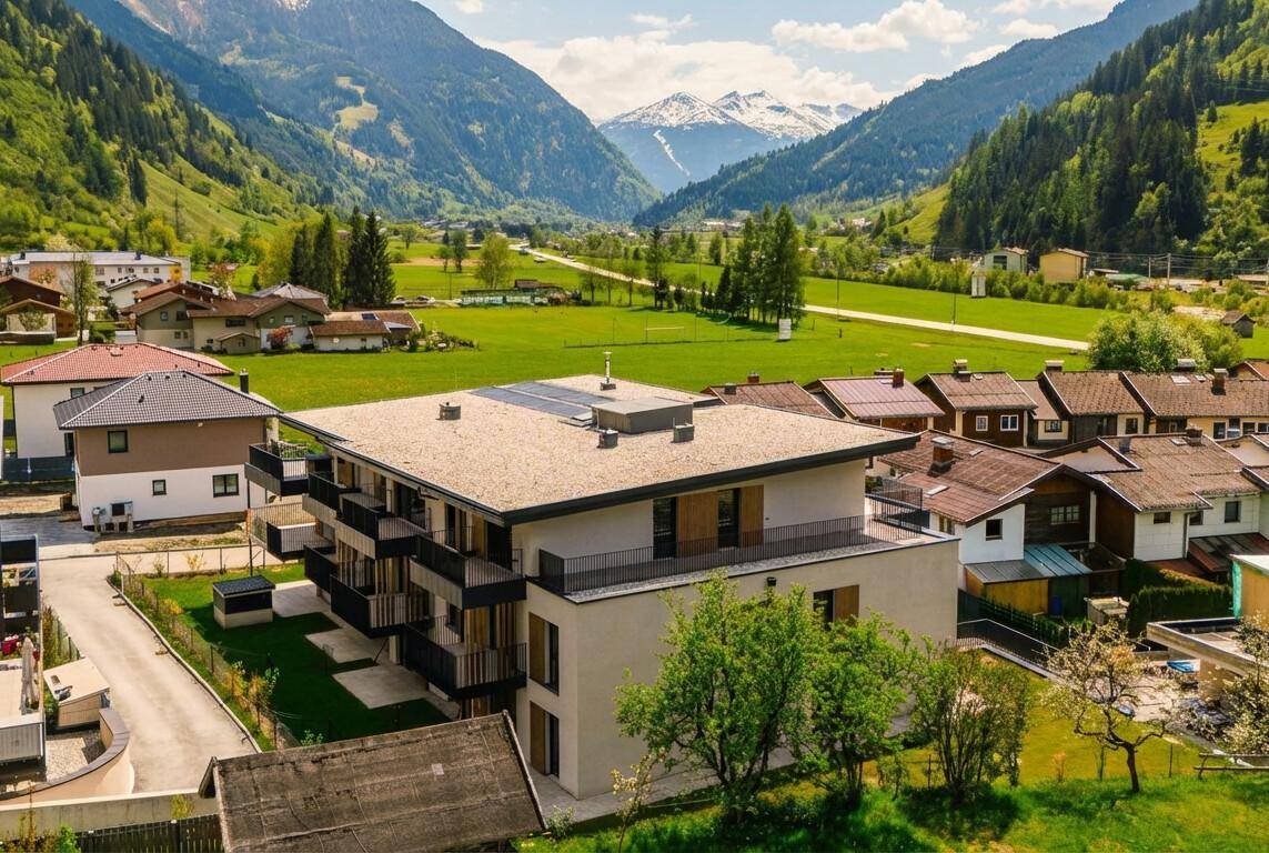 Luftaufnahme eines modernen Wohnkomplexes mit Flachdach und Balkonen in einer idyllischen Bergregion.
