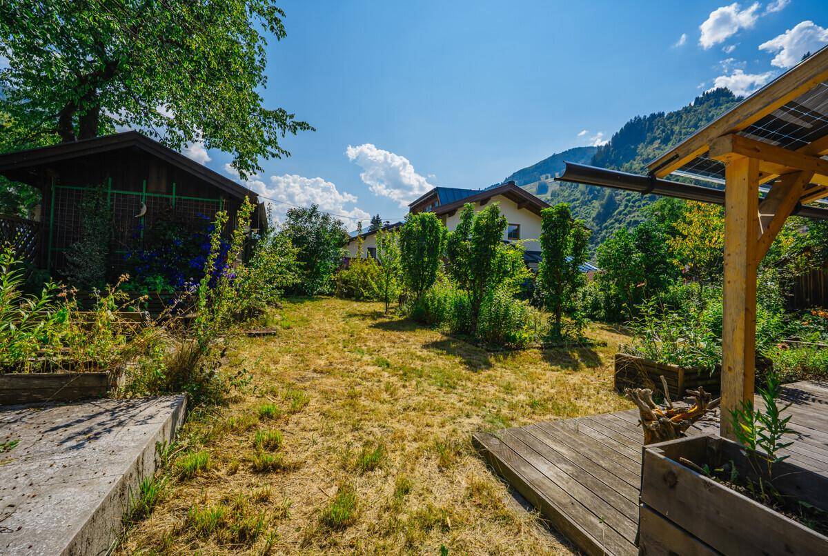Großer Garten mit Holzterrasse, Gartenhaus und Blick auf die umliegende Berglandschaft.