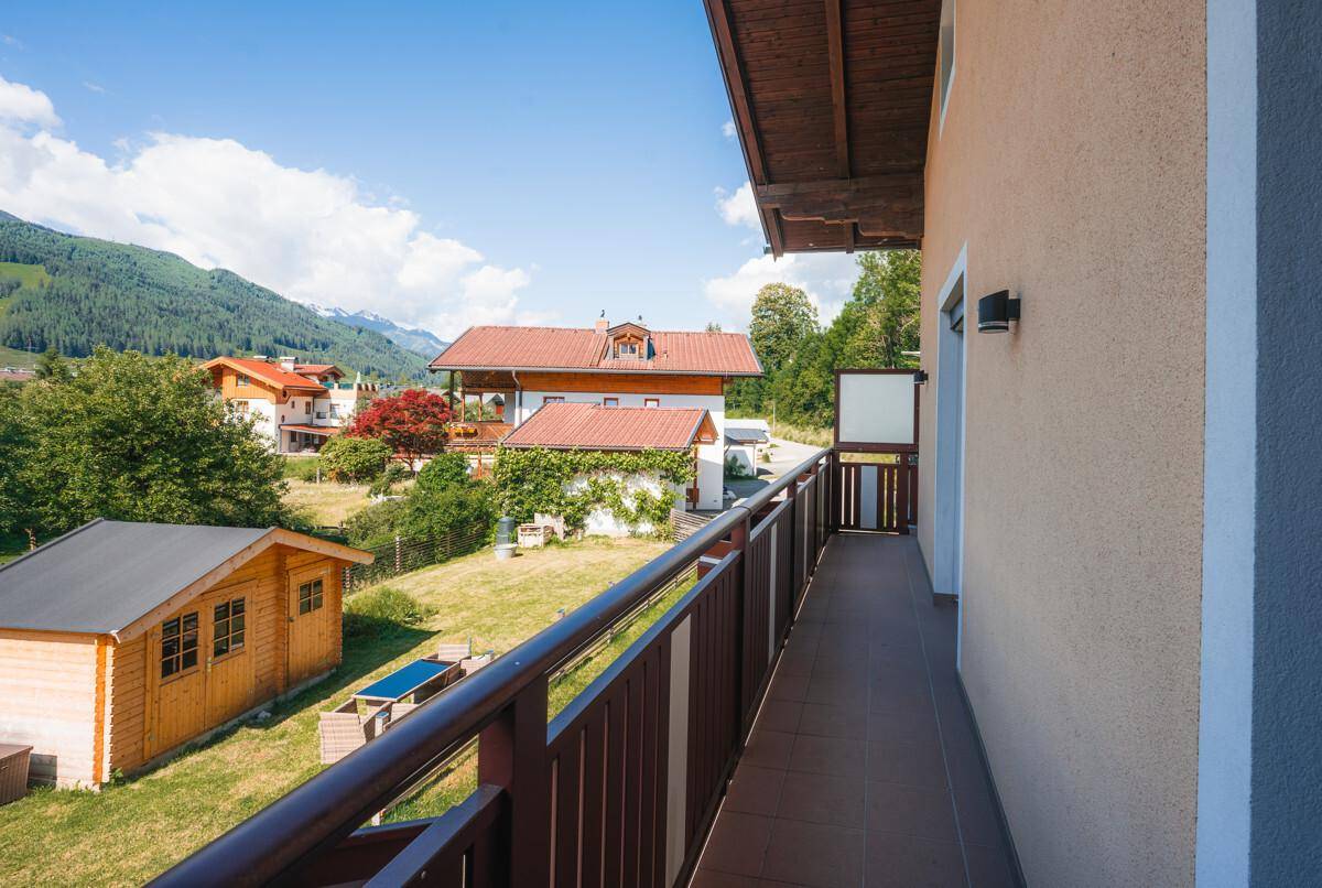 Balkon mit Holzgeländer und weitem Blick auf die grüne Landschaft und ein Gartenhaus.