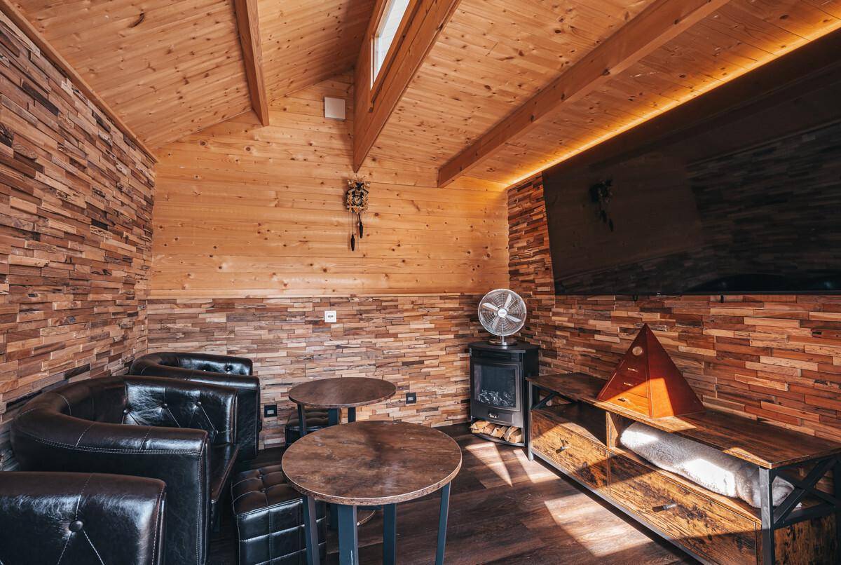 Rustikaler Aufenthaltsraum mit Holzwänden, Ledersesseln und Fernseher.