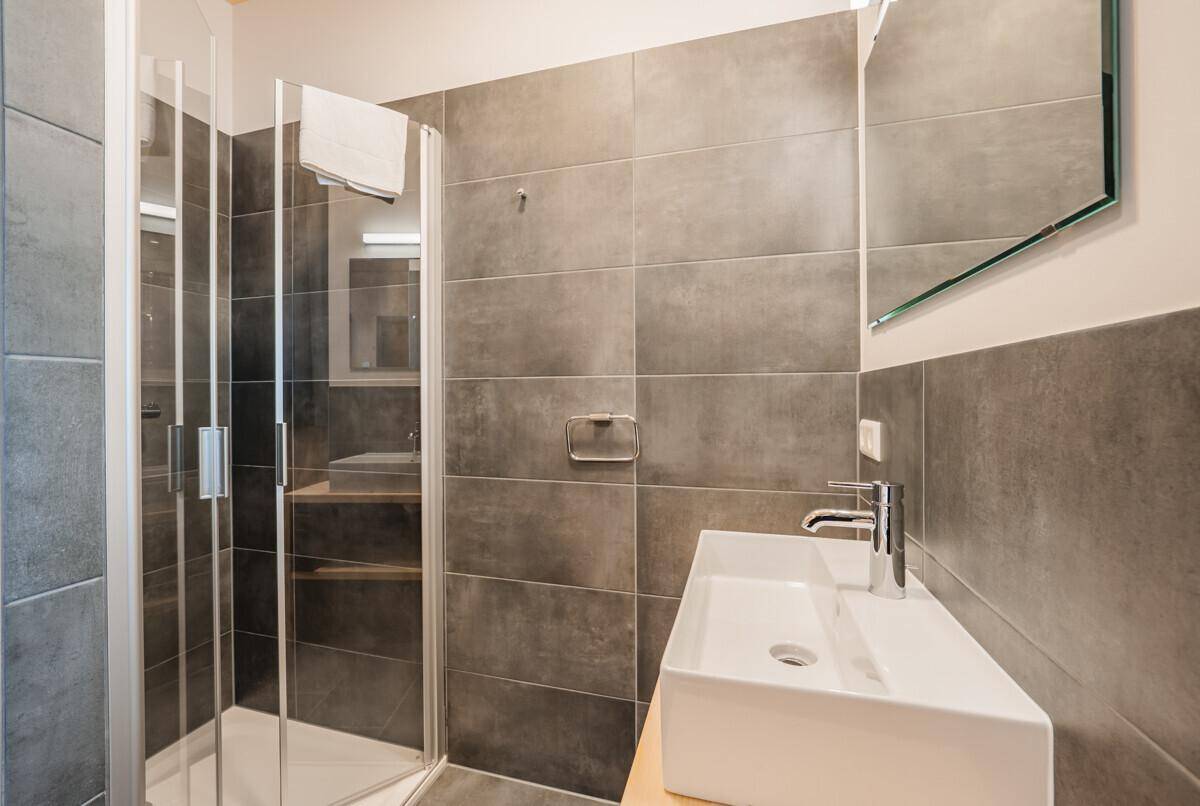 Modernes Badezimmer mit grauen Fliesen, begehbarer Dusche und elegantem Waschbecken.