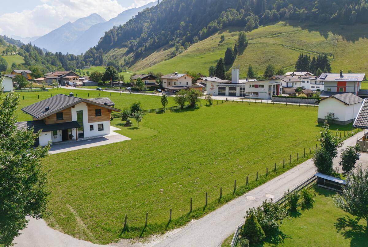 Weitläufige Ansicht von Wohnhäusern und grünen Feldern mit einer beeindruckenden Bergkette im Hintergrund.
