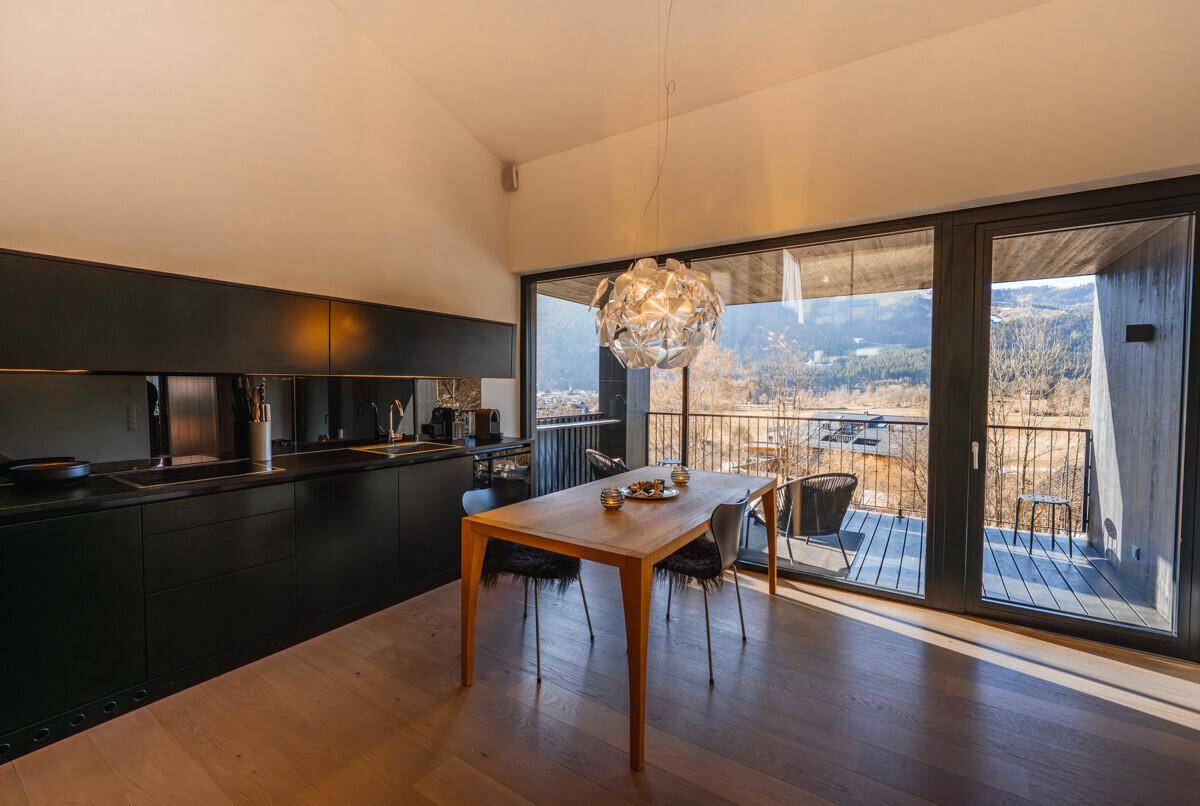 Heller Essbereich mit Holztisch, schwarzer Küche und Zugang zu einem Balkon mit Aussicht.