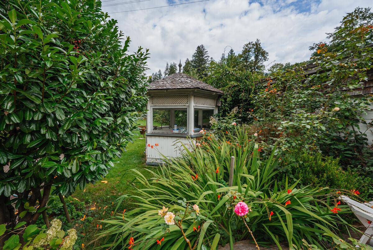 Idyllischer Gartenbereich mit einem weißen Pavillon, umgeben von üppiger Vegetation und Blumen.