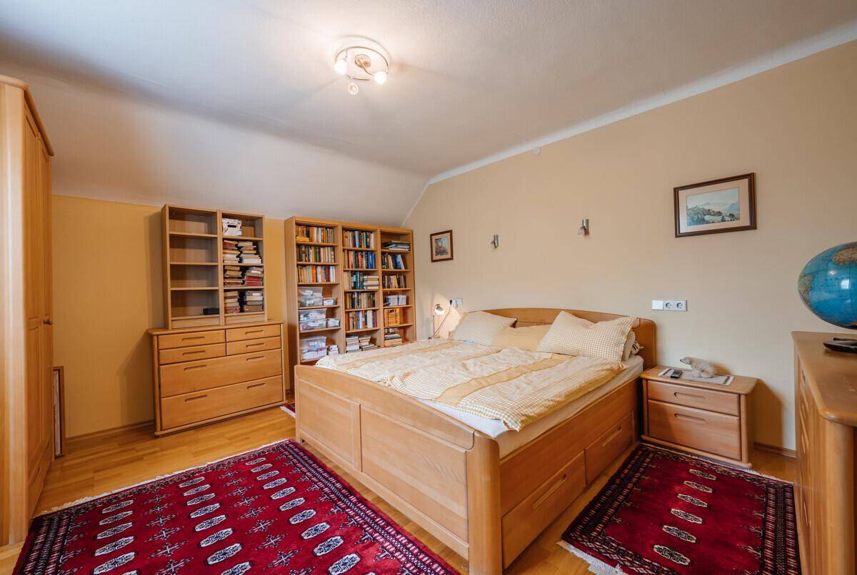 Schlafzimmer mit Holzbett, Bücherregalen und Teppichen, das eine gemütliche Atmosphäre schafft.
