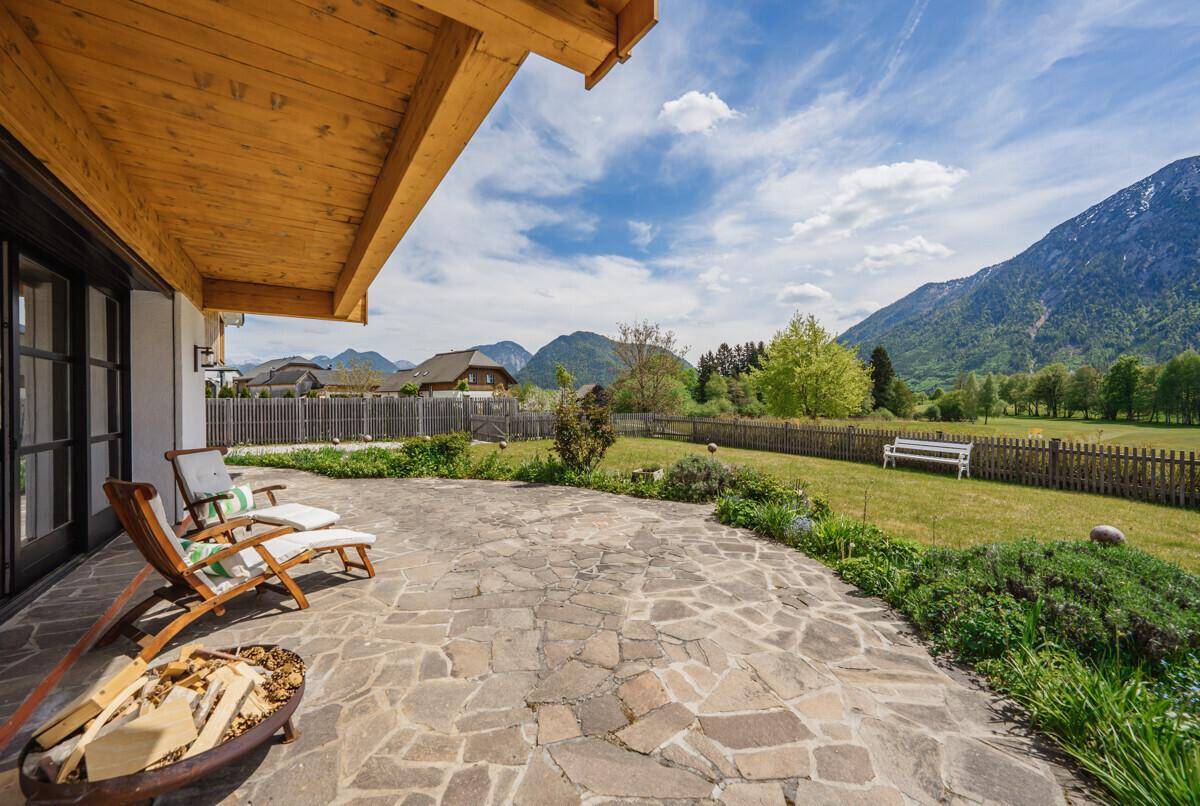 Große Steinterrasse mit Feuerstelle und Zugang zum Garten, umgeben von alpiner Natur.
